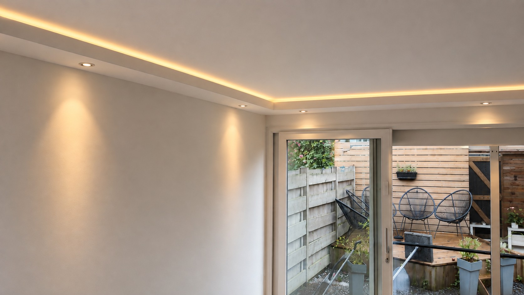 Verlaagd plafond met rondlopende koof, warme LED-lijn en inbouwspots bij tuindeuren